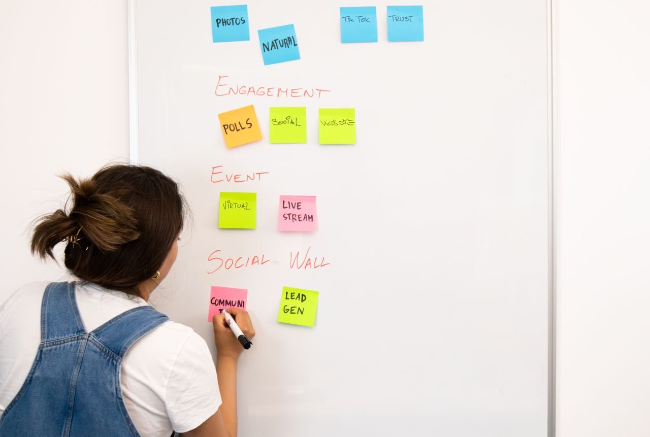 A woman arranging colorful sticky notes on a whiteboard in an office trying to figure out what to automate