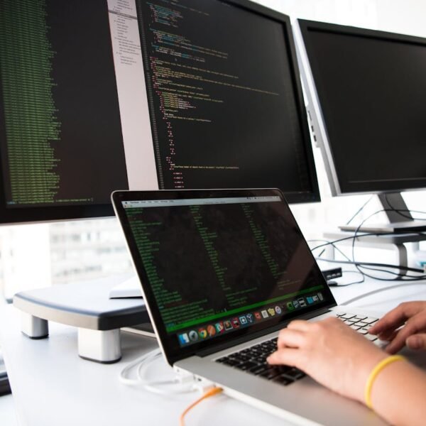 Close-up of a developer typing on a laptop with code visible on multiple monitors in the background, illustrating the technical and content work behind AI search optimization for a small business.