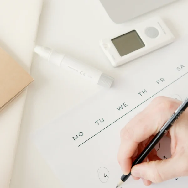Hand marking dates on a paper calendar next to a laptop, illustrating the shift from manual scheduling to automated appointment booking for small businesses.