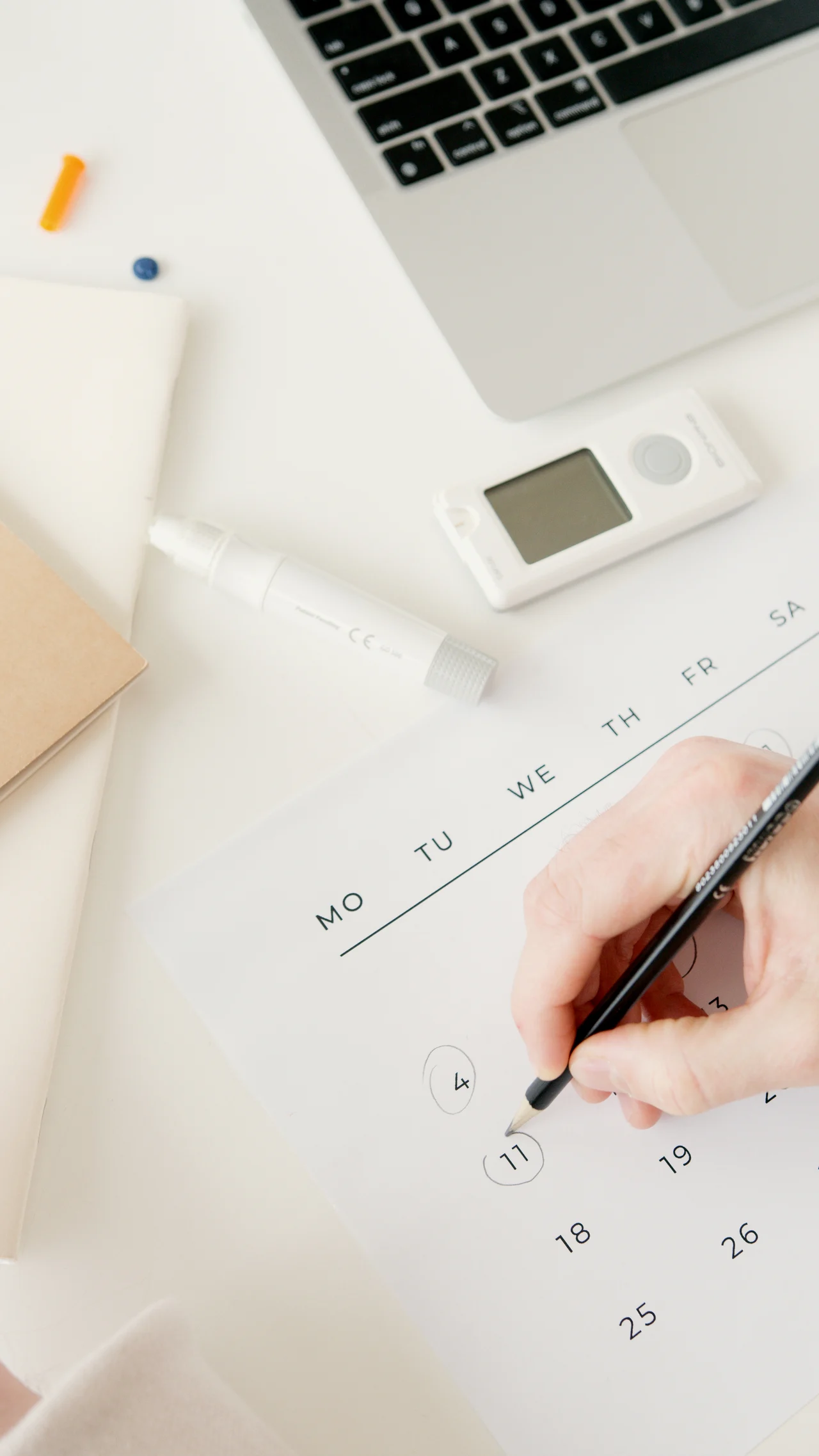 Hand marking dates on a paper calendar next to a laptop, illustrating the shift from manual scheduling to automated appointment booking for small businesses.
