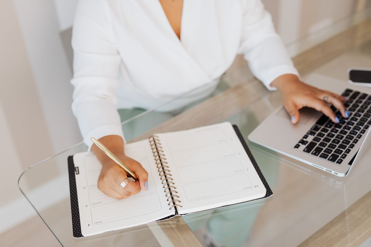 Small business owner reviewing a printed task list beside a laptop while prioritizing work