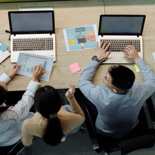 Three coworkers reviewing laptops and printed reports together at an office desk