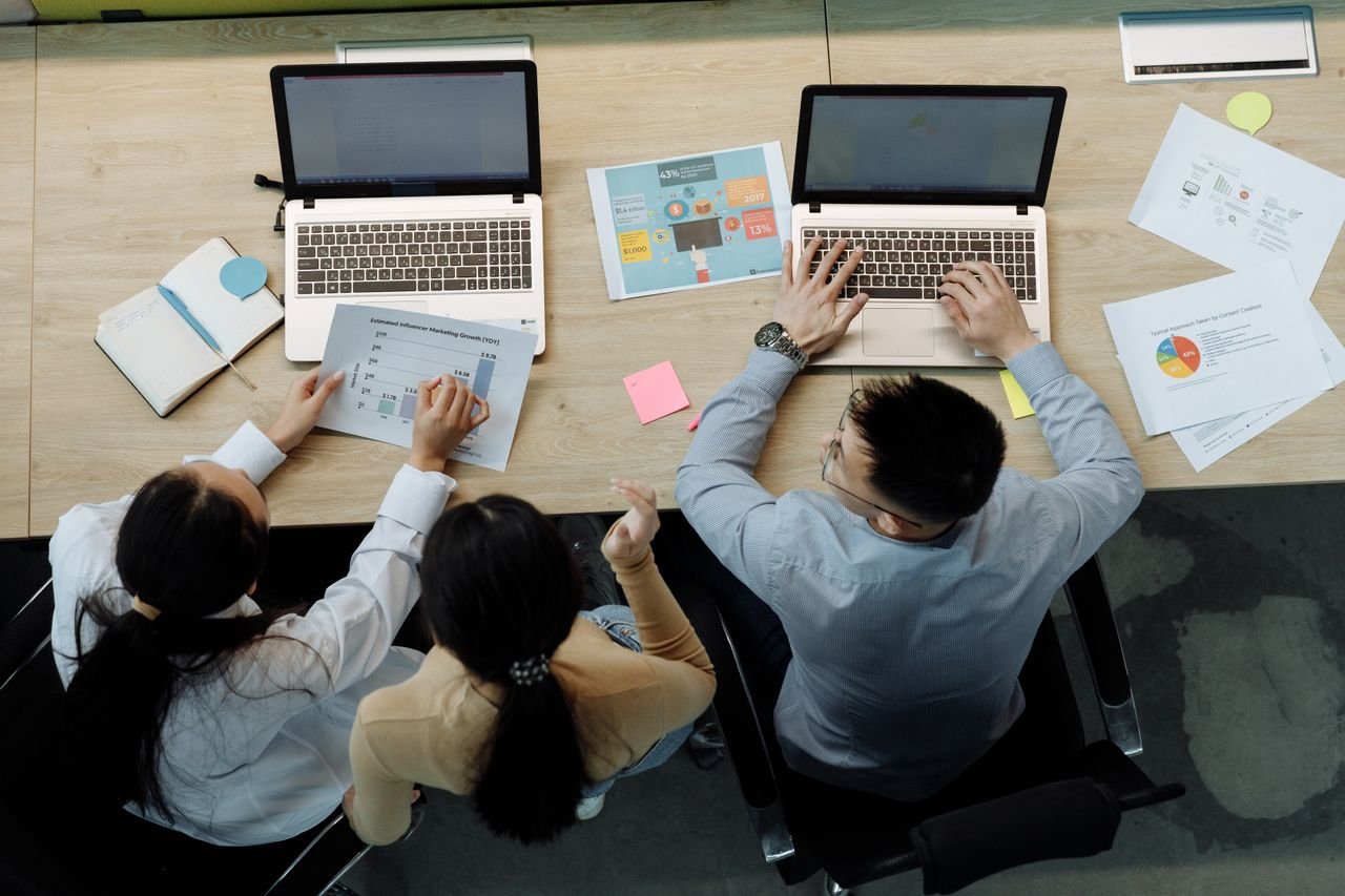 Three coworkers reviewing laptops and printed reports together at an office desk