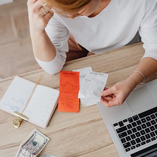 Person at a desk reviewing paper receipts beside a laptop and notebook while planning a budget