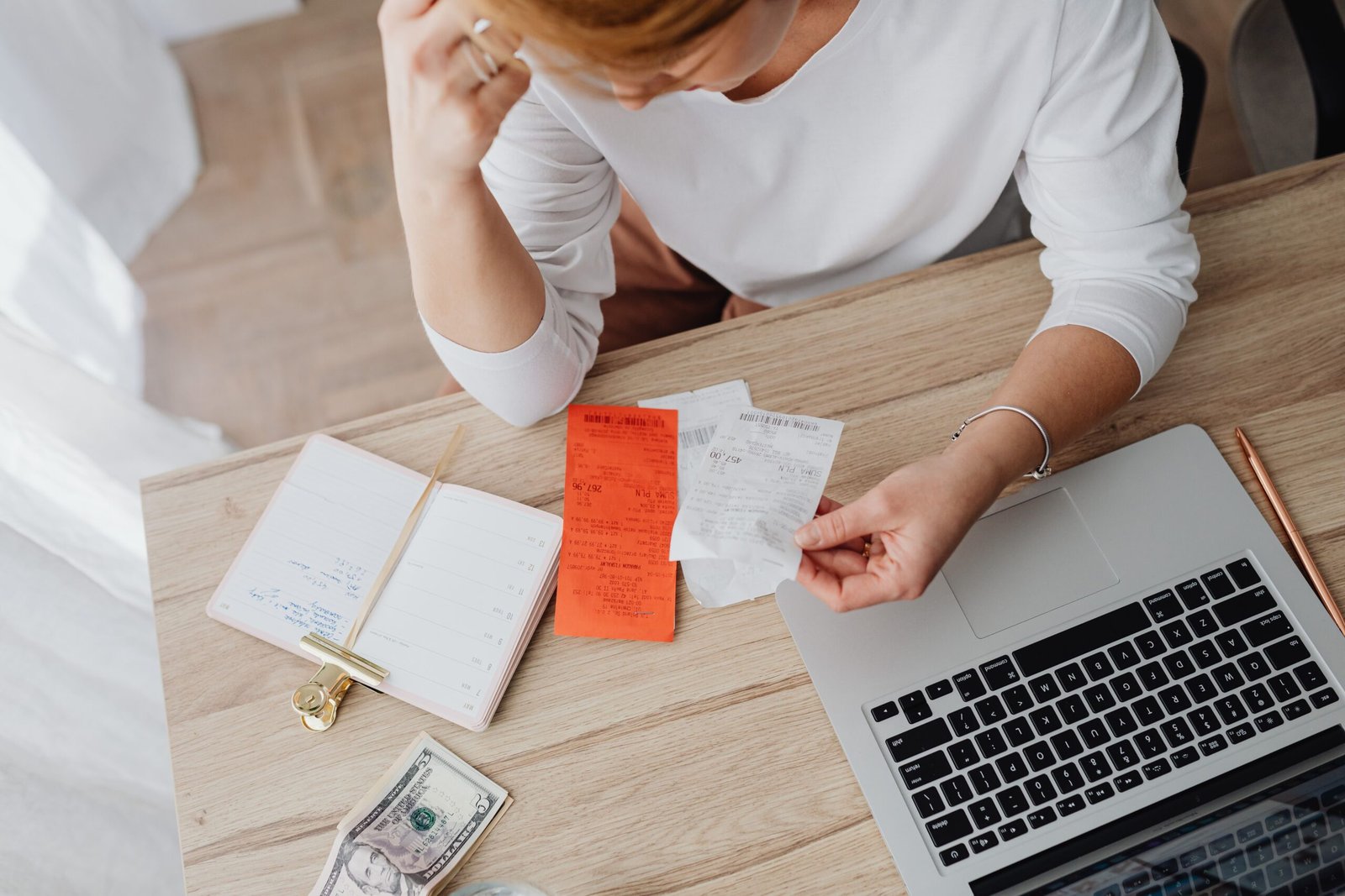 Person at a desk reviewing paper receipts beside a laptop and notebook while planning a budget