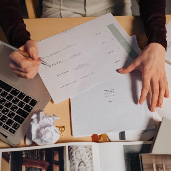 A person takes notes at a desk with a laptop and printed documents spread out in front of them...Looking at AI policies.